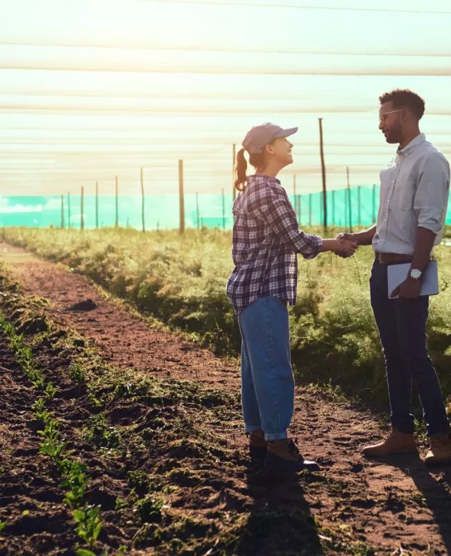 Full length shot of two young farmers shaking hands while working on their farm.
